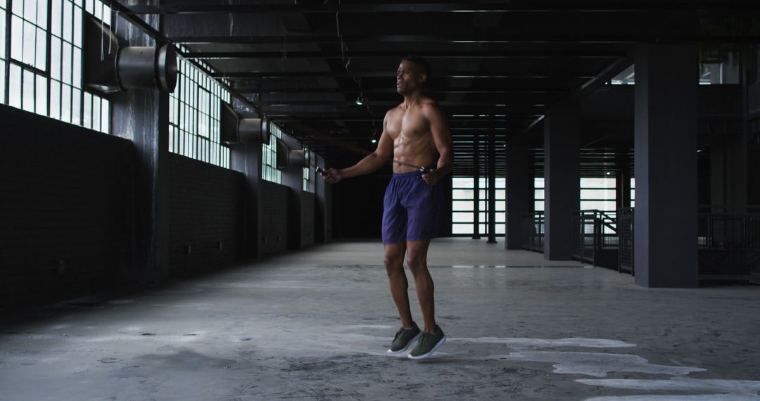 Shirtless african american man skipping the rope in an empty urban building - Free Images, Stock Photos and Pictures on Pikwizard.com