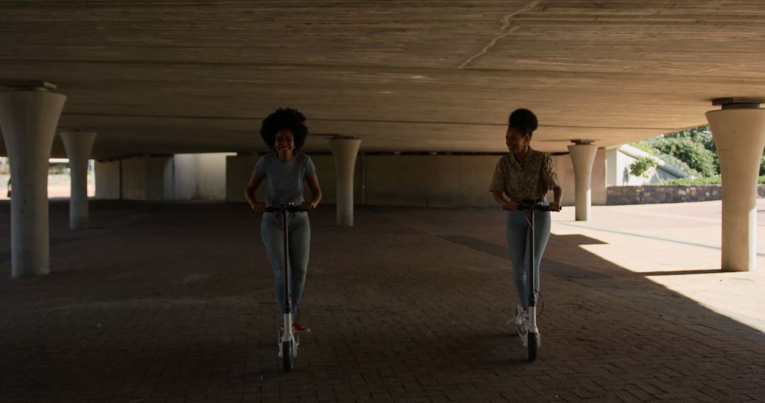 Two Young Women Riding Electric Scooters Under Bridge - Free Images, Stock Photos and Pictures on Pikwizard.com