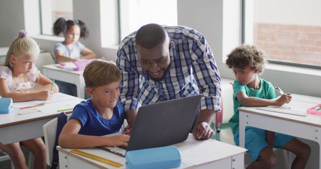 Image of happy african american male teacher helping caucasian boy with laptop - Free Images, Stock Photos and Pictures on Pikwizard.com