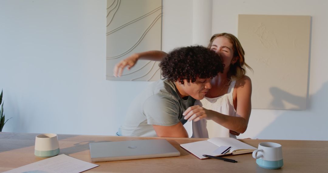 Joyful Couple Embracing at Home with Laptop and Notebooks