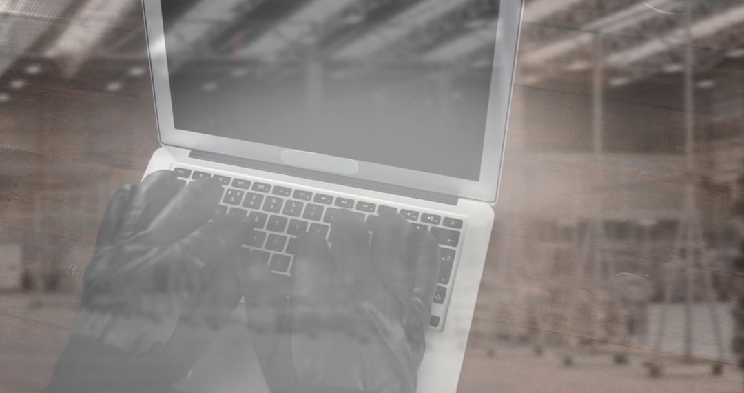 Gloved Intruder Typing on Laptop in Warehouse Environment