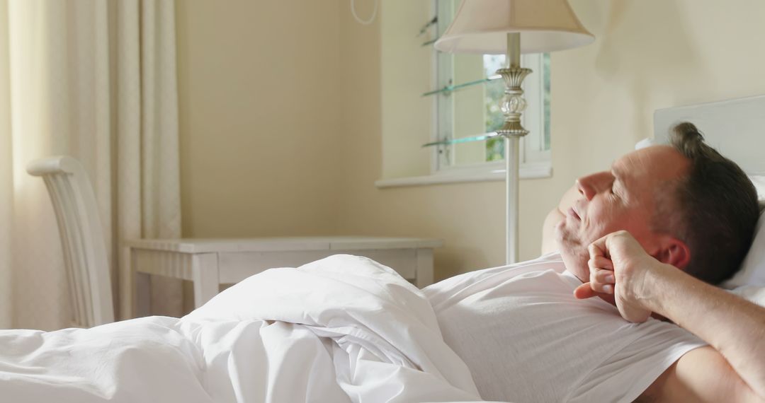 Middle-aged man stretching in bed after waking up in bright bedroom - Free Images, Stock Photos and Pictures on Pikwizard.com