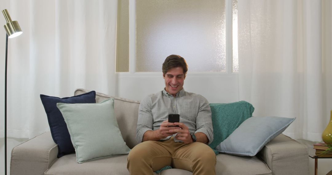 Happy Man Smiling While Using Smartphone on Couch at Home - Free Images, Stock Photos and Pictures on Pikwizard.com