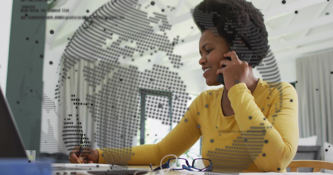 Professional woman talking on smartphone while working at laptop with global digital overlay