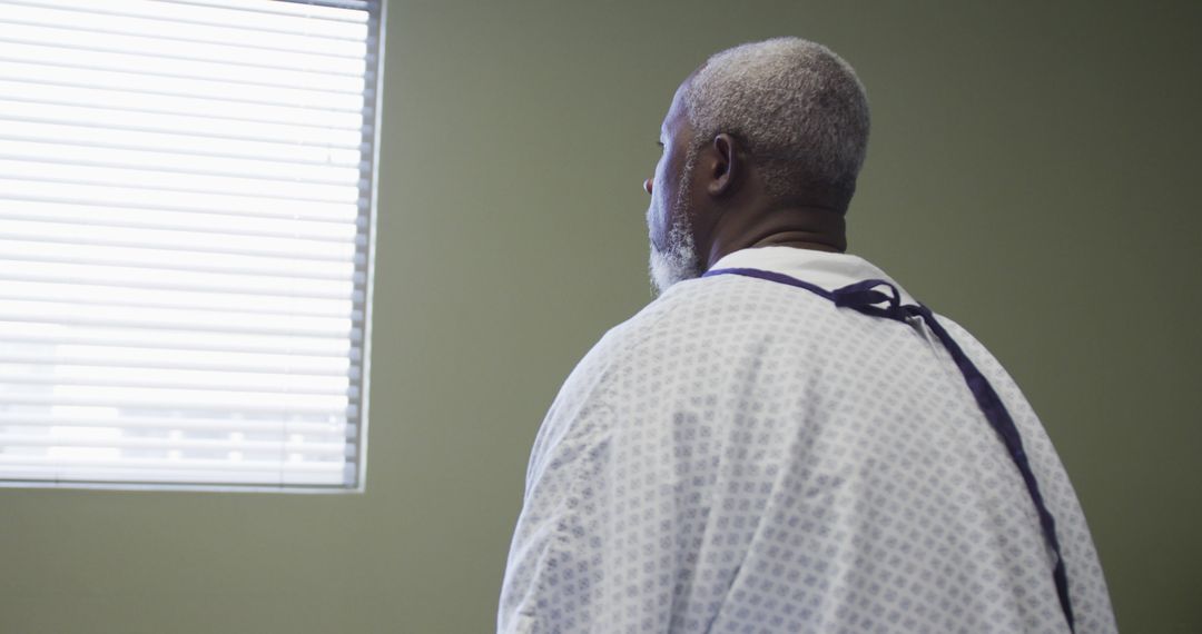 Older Male Patient In Hospital Gown Looking Out Window - Free Images, Stock Photos and Pictures on Pikwizard.com