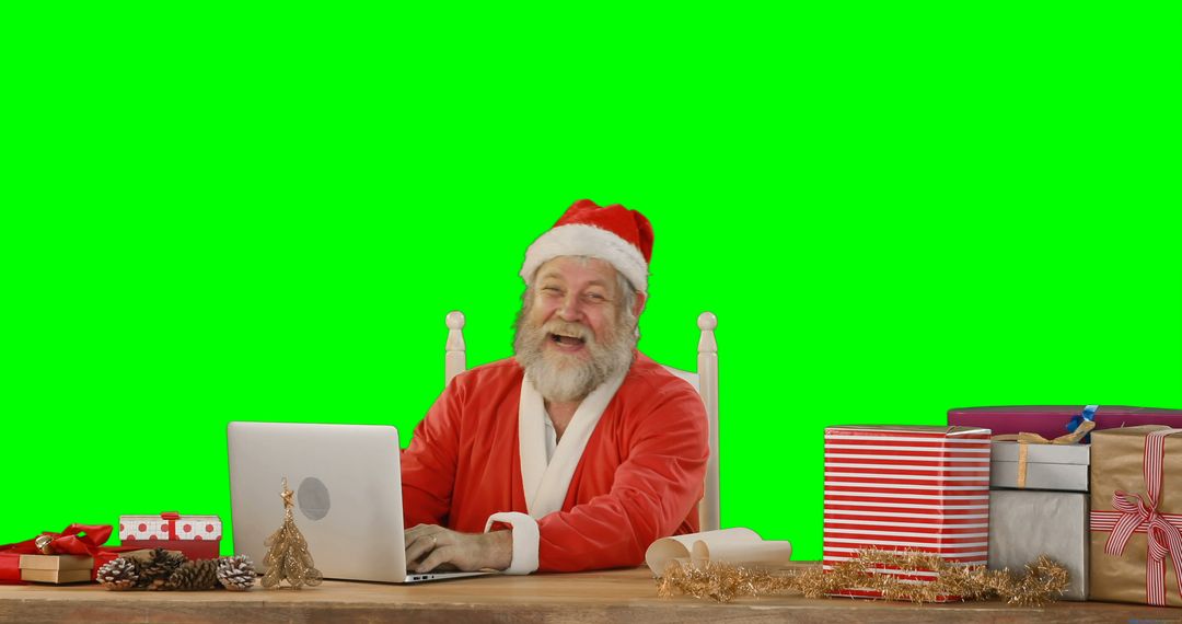 Santa Claus cheerfully using laptop surrounded by Christmas gifts - Free Images, Stock Photos and Pictures on Pikwizard.com