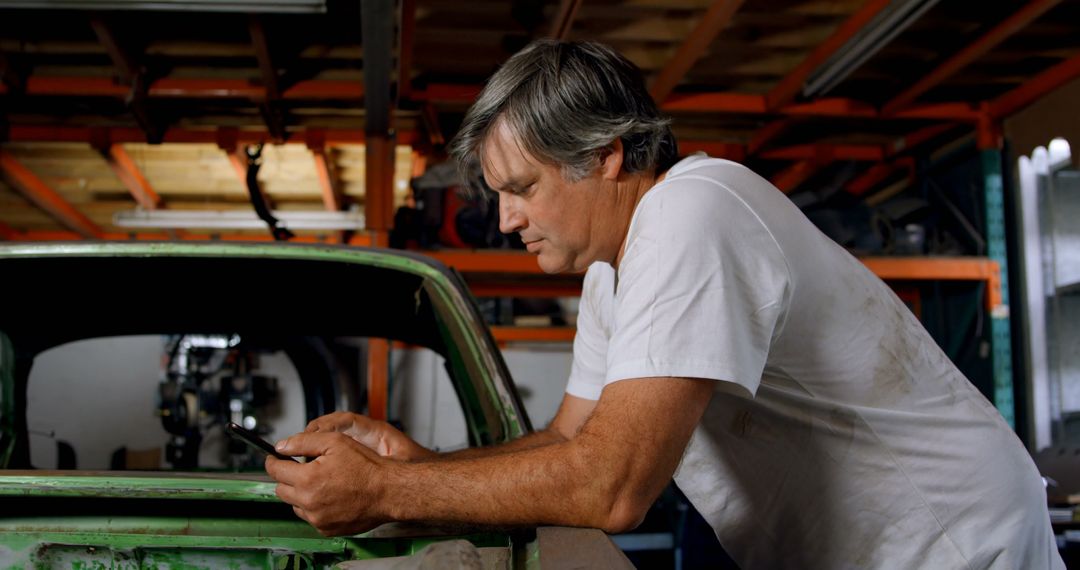 Middle-Aged Mechanic Leaning on Car in Garage using Smartphone - Free Images, Stock Photos and Pictures on Pikwizard.com