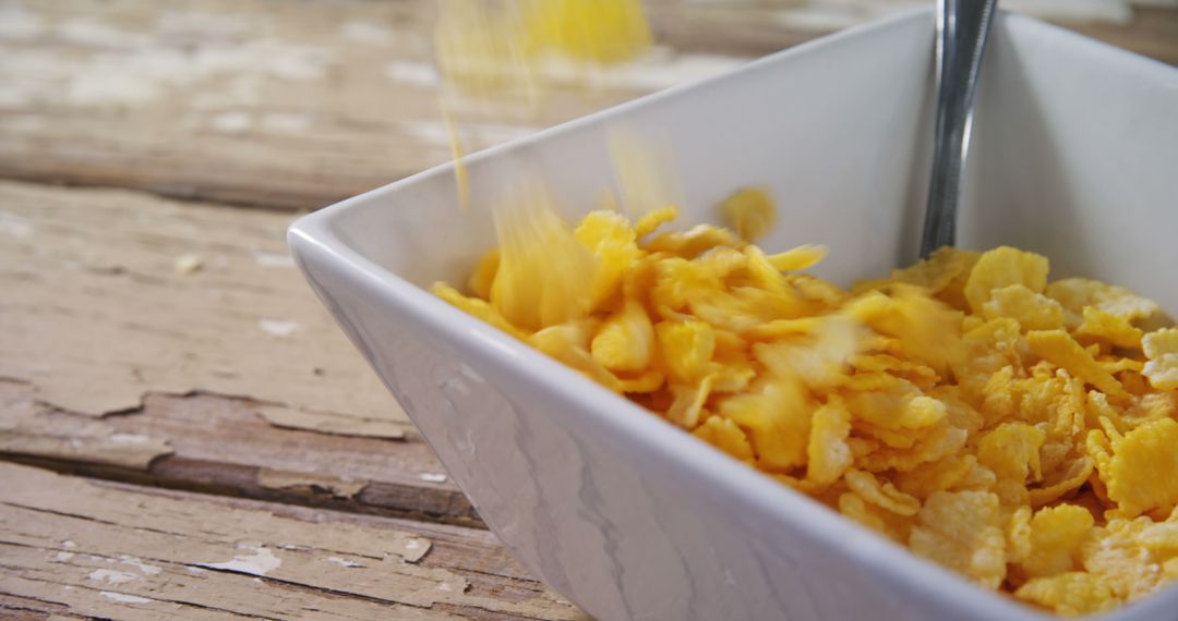 Close-up of Cornflakes Falling into White Bowl on Rustic Wooden Table - Free Images, Stock Photos and Pictures on Pikwizard.com