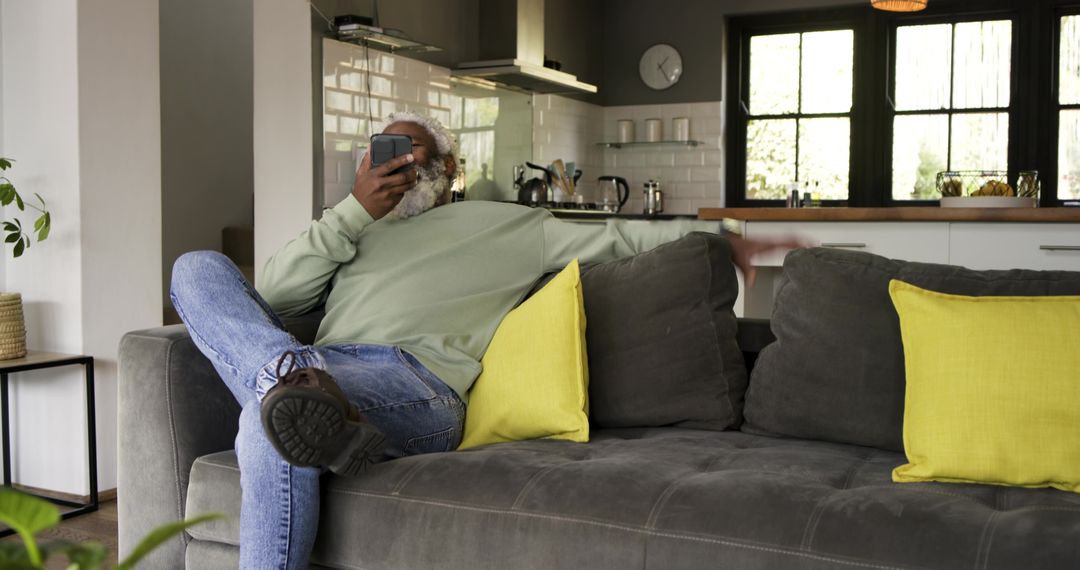 Middle-aged Man Relaxing with Smartphone on Modern Sofa in Urban Kitchen