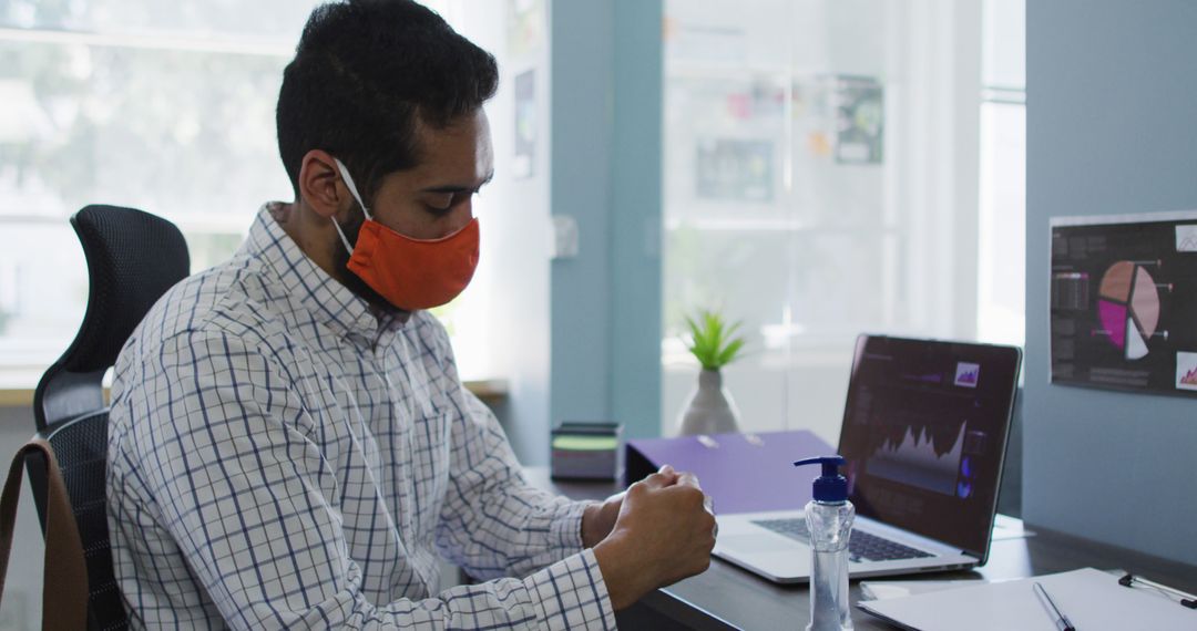 Office Worker Wearing Mask Using Hand Sanitizer at Desk - Free Images, Stock Photos and Pictures on Pikwizard.com