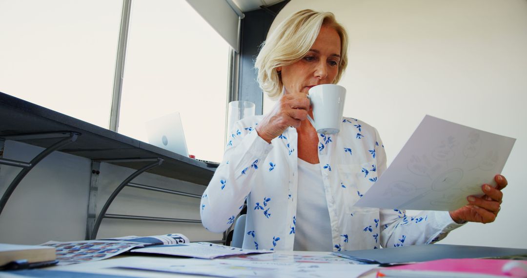 Senior Woman Reading Document While Drinking Coffee in Office - Free Images, Stock Photos and Pictures on Pikwizard.com