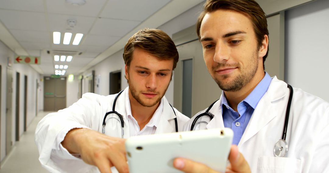 Doctors Discussing Patient Data on Tablet in Hospital Corridor - Free Images, Stock Photos and Pictures on Pikwizard.com