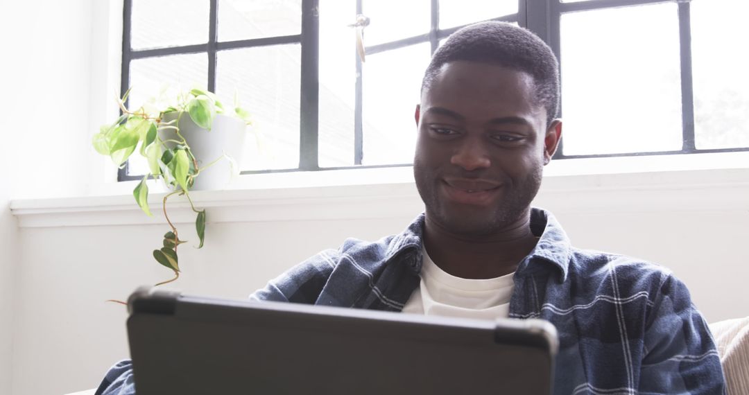 Man Relaxing on Sofa with Tablet Near Window Plant
