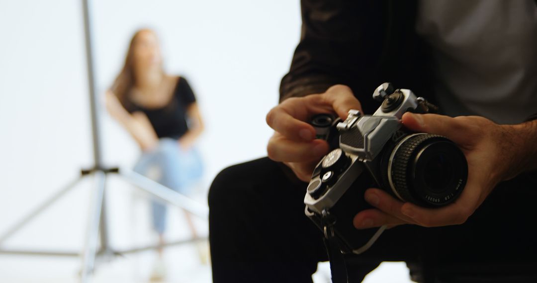 Photographer Adjusting Camera Settings in Studio with Model in Background - Free Images, Stock Photos and Pictures on Pikwizard.com