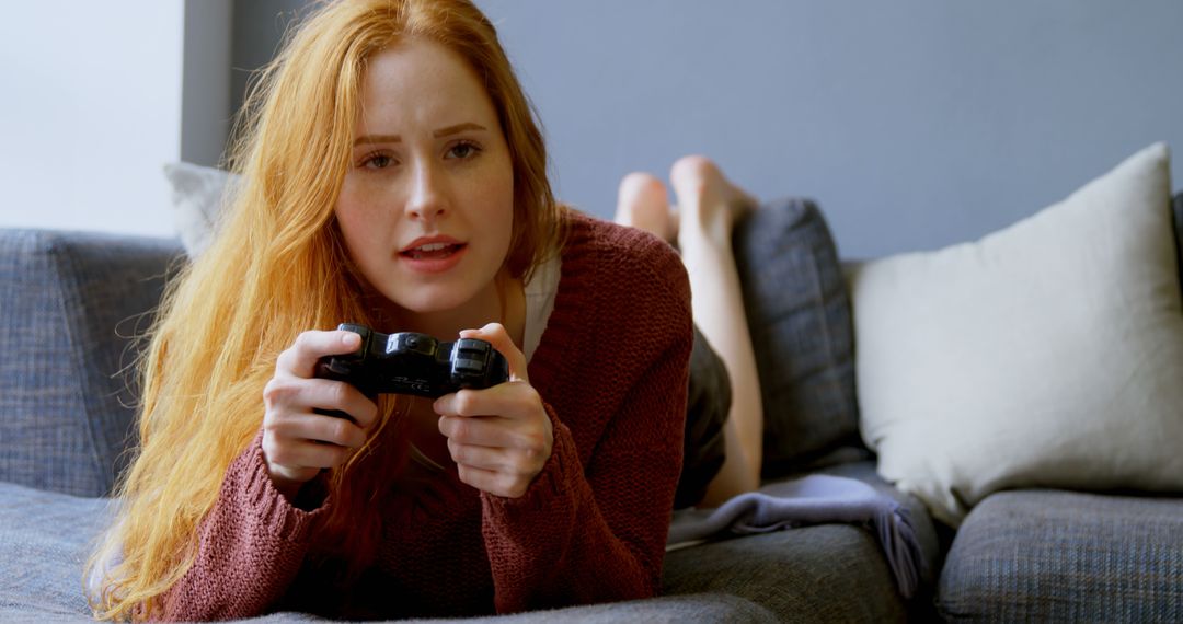 Young Caucasian woman enjoys gaming on the couch at home - Free Images, Stock Photos and Pictures on Pikwizard.com