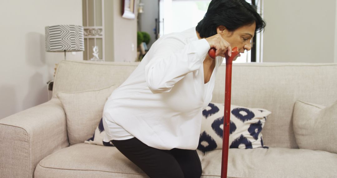 Senior Woman Using Cane to Stand from Sofa Indoors - Free Images, Stock Photos and Pictures on Pikwizard.com