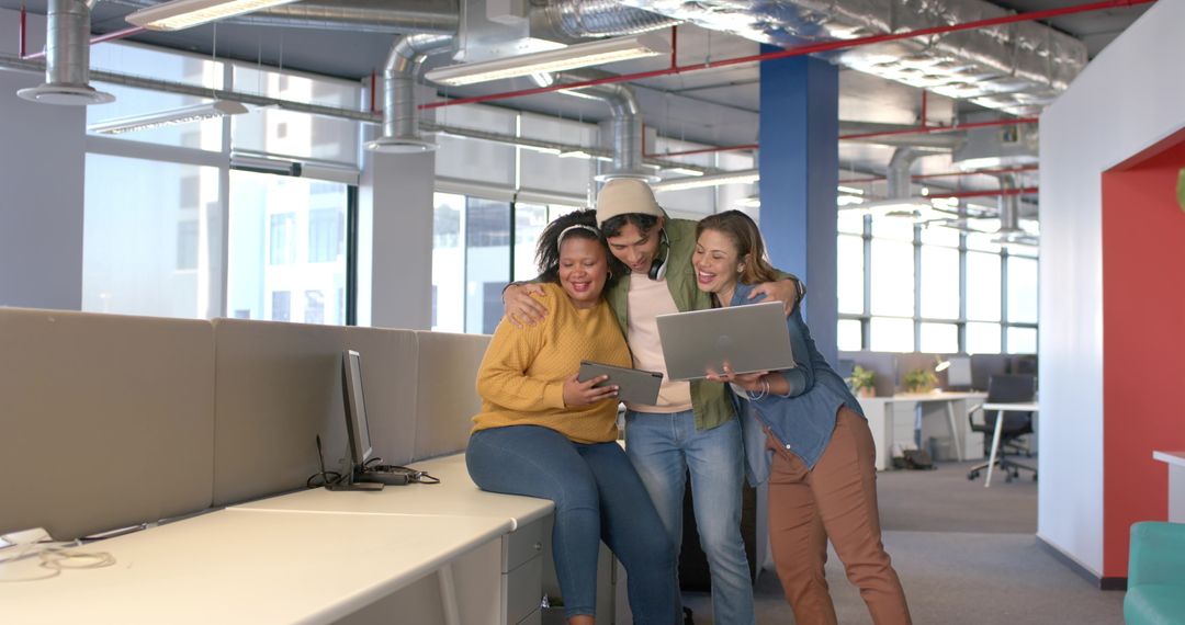 Diverse team collaborating and smiling while viewing tablet and laptop in bright office