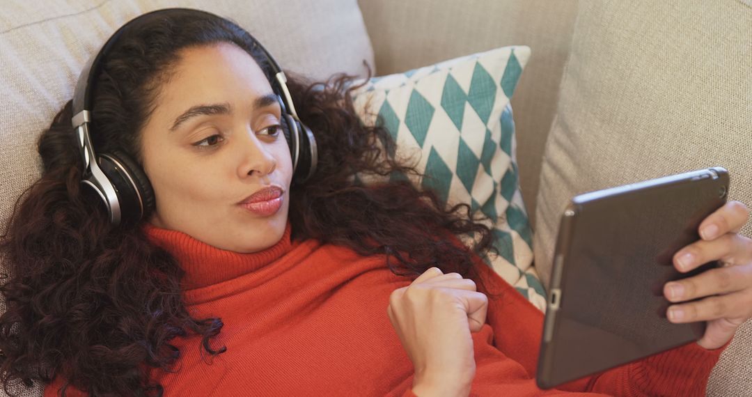 Woman Relaxing on Couch Watching Tablet and Listening with Headphones - Free Images, Stock Photos and Pictures on Pikwizard.com