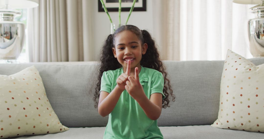 Happy biracial girl sitting on sofa using sign language - Free Images, Stock Photos and Pictures on Pikwizard.com