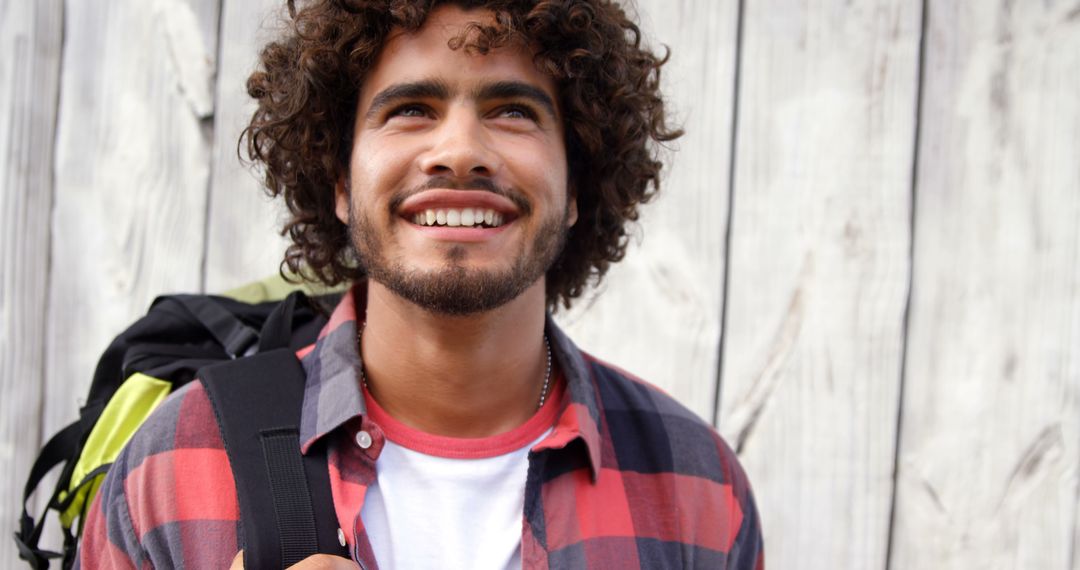 Happy biracial man with curly hair standing and smiling by wooden wall on sunny day, copy space - Free Images, Stock Photos and Pictures on Pikwizard.com