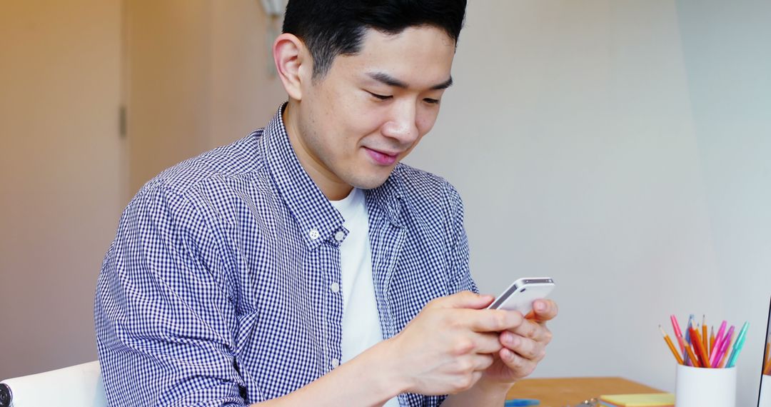 Young Man Smiling and Using Smartphone at Desk - Free Images, Stock Photos and Pictures on Pikwizard.com