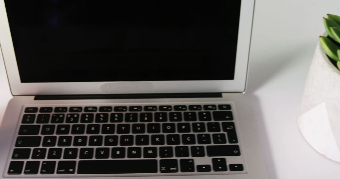 A laptop with a black screen sits on a white surface next to a potted plant, with copy space - Free Images, Stock Photos and Pictures on Pikwizard.com