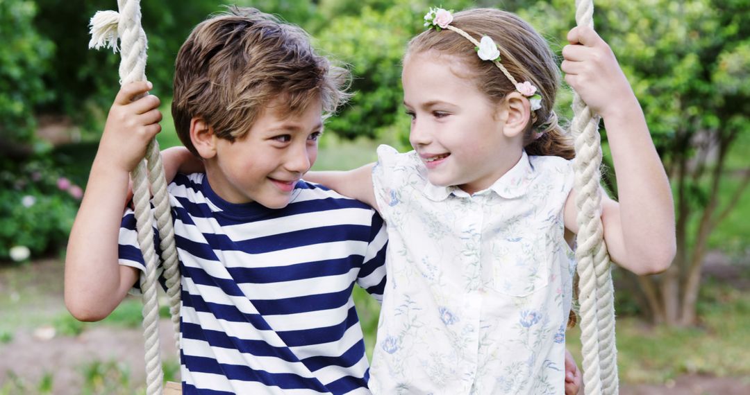 A young Caucasian boy and girl enjoy a playful moment on a swing in a lush garden, with copy space - Free Images, Stock Photos and Pictures on Pikwizard.com