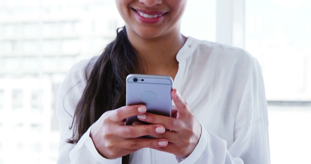 Woman Smiling While Typing on Smartphone Indoors - Free Images, Stock Photos and Pictures on Pikwizard.com