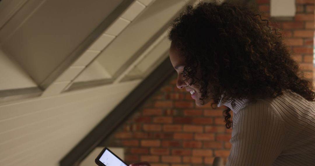 Woman Smiling While Using Smartphone in Cozy Attic - Free Images, Stock Photos and Pictures on Pikwizard.com