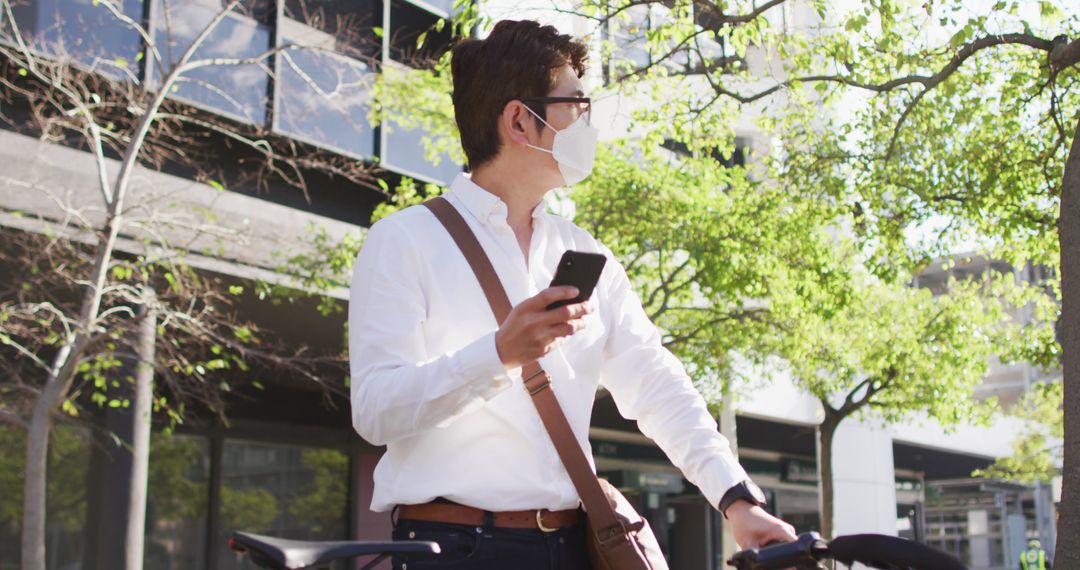 Young Professional Man Wearing Face Mask Looking at Smartphone Outside Office Building - Free Images, Stock Photos and Pictures on Pikwizard.com