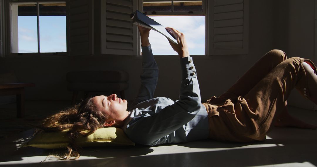 Young Woman Reading Book on Floor by Sunlit Window - Free Images, Stock Photos and Pictures on Pikwizard.com