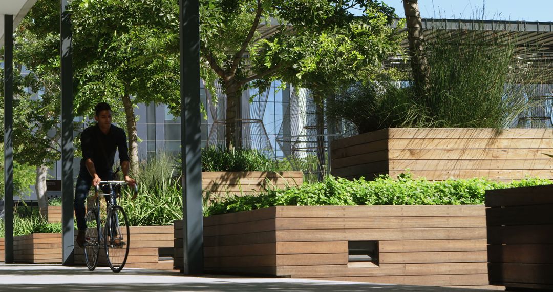 Man riding bicycle through modern urban park with wooden planters - Free Images, Stock Photos and Pictures on Pikwizard.com