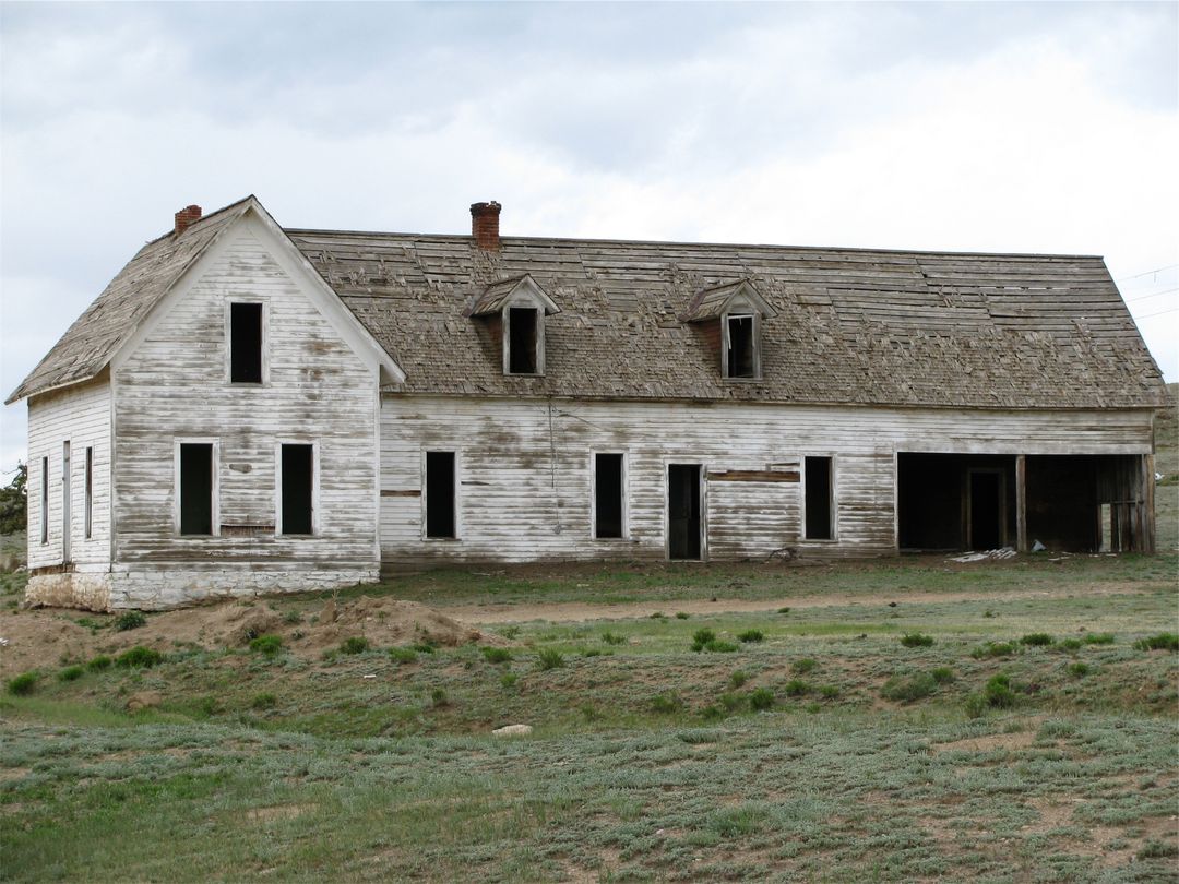 Weathered Abandoned Farmhouse with Peeling White Paint and Broken Windows on Open Prairie