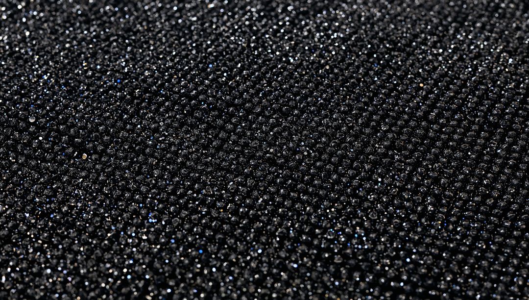 Macro glittering black bead texture on dark fabric, sparkling granular shimmering pattern