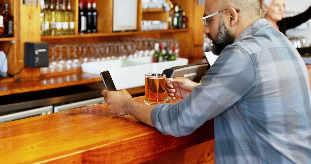 Middle-Aged Man Relaxing at Bar with Smartphone and Drink
