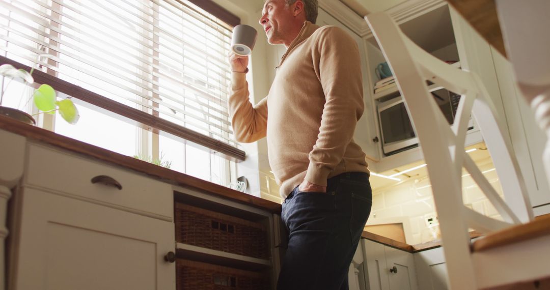 Man Drinking Coffee While Looking Out Window in Warm Kitchen - Free Images, Stock Photos and Pictures on Pikwizard.com