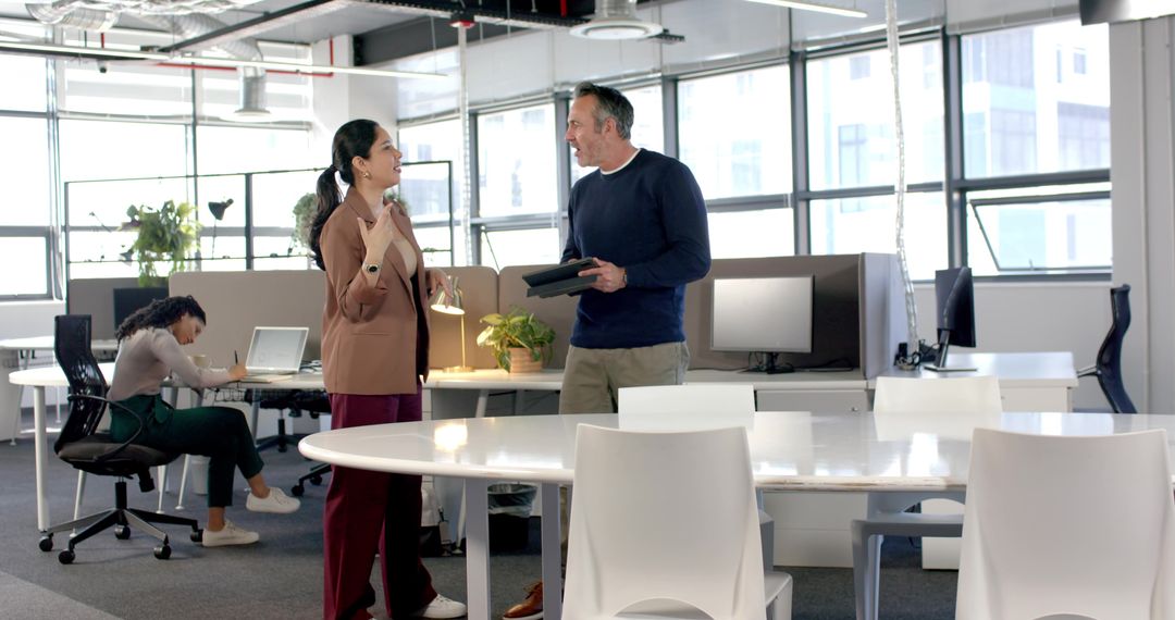Diverse colleagues discussing and collaborating in modern open-plan office with tablet