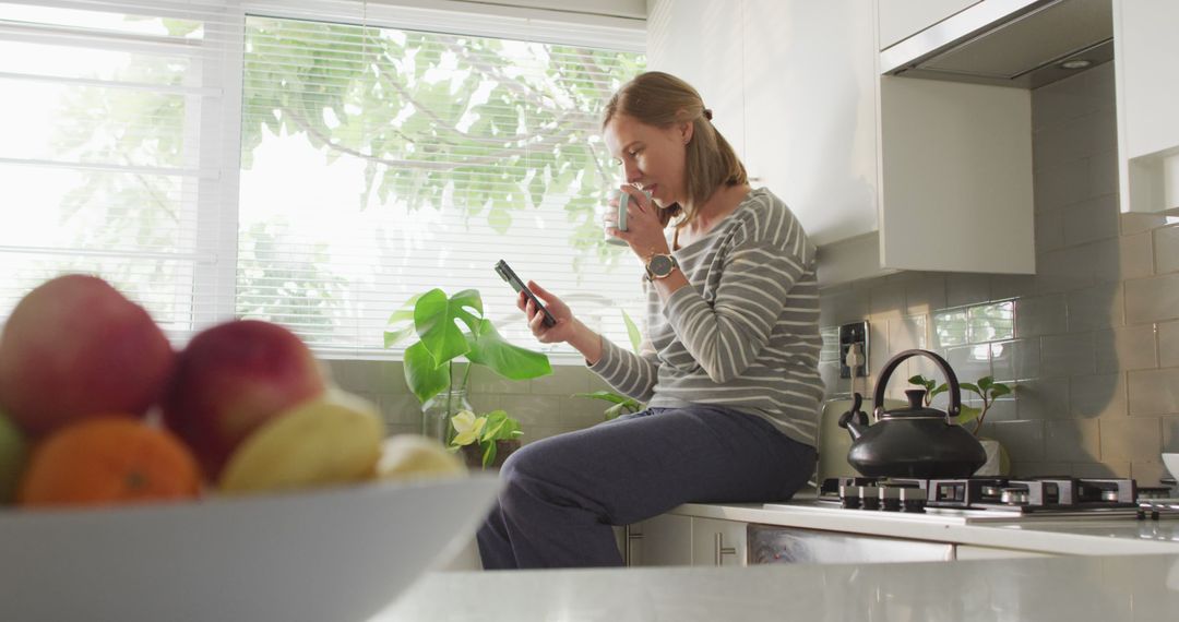 Relaxed Woman Drinking Coffee and Using Smartphone in Modern Kitchen - Free Images, Stock Photos and Pictures on Pikwizard.com