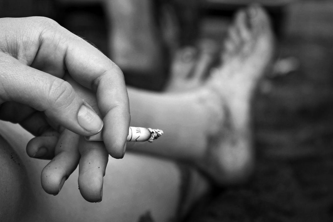 Close-up of Hand Holding Cigarette with Bare Feet in Background - Free Images, Stock Photos and Pictures on Pikwizard.com