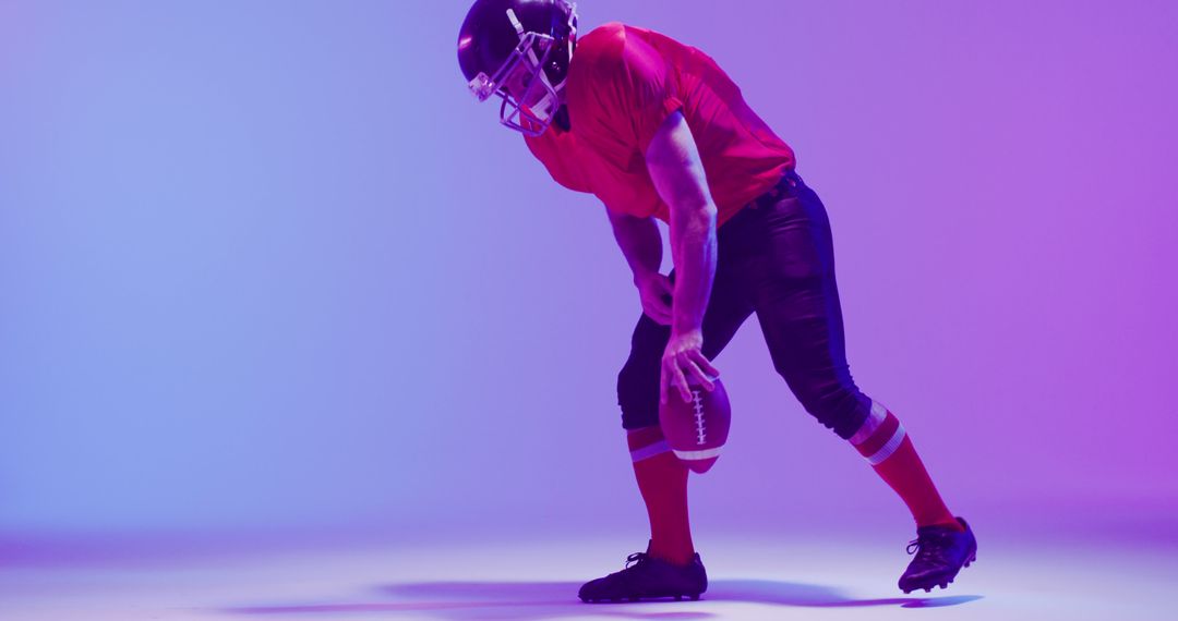 A football player kneels with a ball against a neon purple backdrop, symbolizing sportsmanship. - Free Images, Stock Photos and Pictures on Pikwizard.com