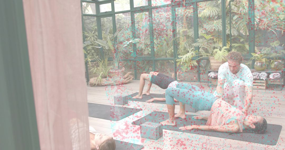 Instructor assisting student in glass studio during group yoga class with blocks and mats