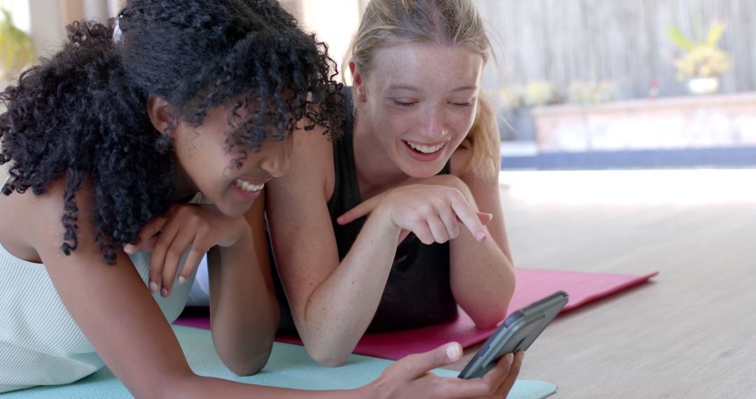 Two Young Women Enjoying Yoga Break Laughing at Mobile Phone - Free Images, Stock Photos and Pictures on Pikwizard.com