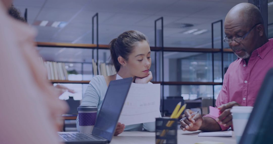 Diverse Office Team Collaborating on Documents at Desk with Laptops