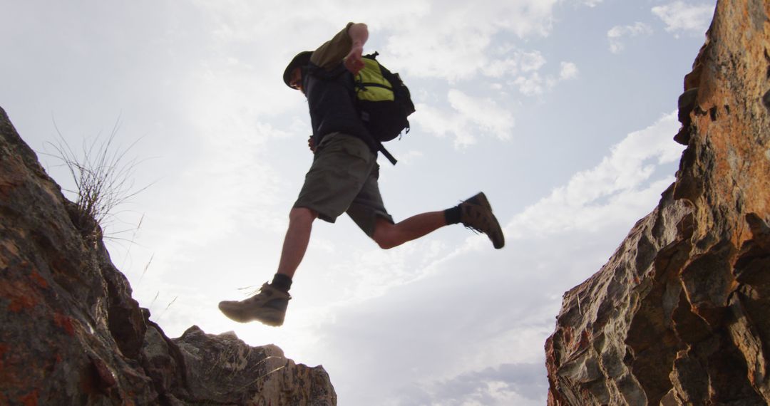 Adventurous Hiker Jumping Over Rocky Ravine in Wilderness