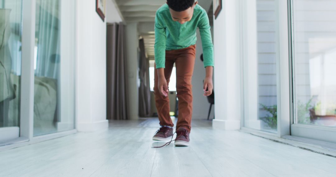 African american boy standing in hallway tying his shoes - Free Images, Stock Photos and Pictures on Pikwizard.com