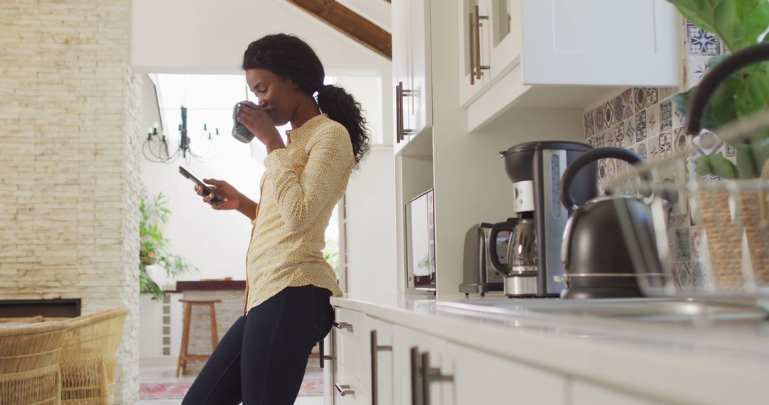 Woman Balancing Coffee and Smartphone in Modern Kitchen - Free Images, Stock Photos and Pictures on Pikwizard.com