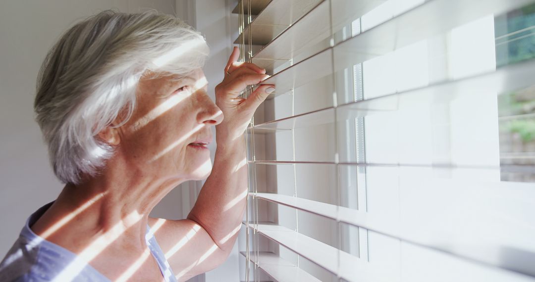 Elderly Woman Looking Out Window Through Blinds with Sunlight - Free Images, Stock Photos and Pictures on Pikwizard.com