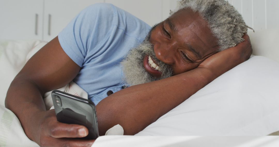 Senior Man Lying in Bed Smiling at Smartphone Screen - Free Images, Stock Photos and Pictures on Pikwizard.com