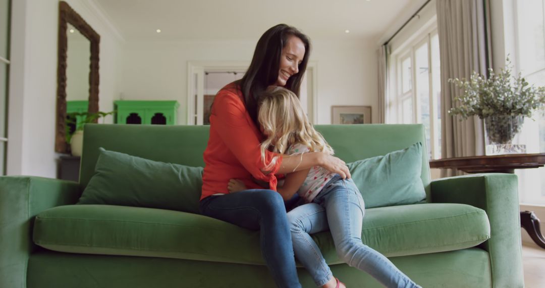 Mother embracing young daughter on green sofa in living room - Free Images, Stock Photos and Pictures on Pikwizard.com