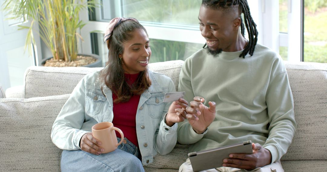 Multicultural couple sharing online payment while relaxing on sunlit living room sofa